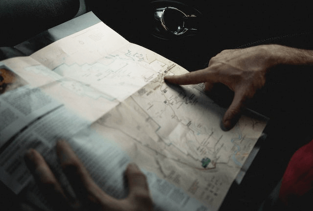 A person follows the road on the paper map in his hand to know his private car service point to point path and directions